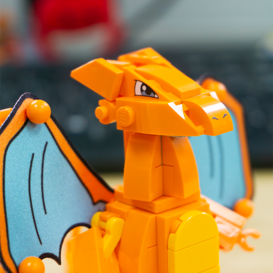 A close-up of an orange toy dragon figure with light blue wings, photographed against a blurred indoor background.