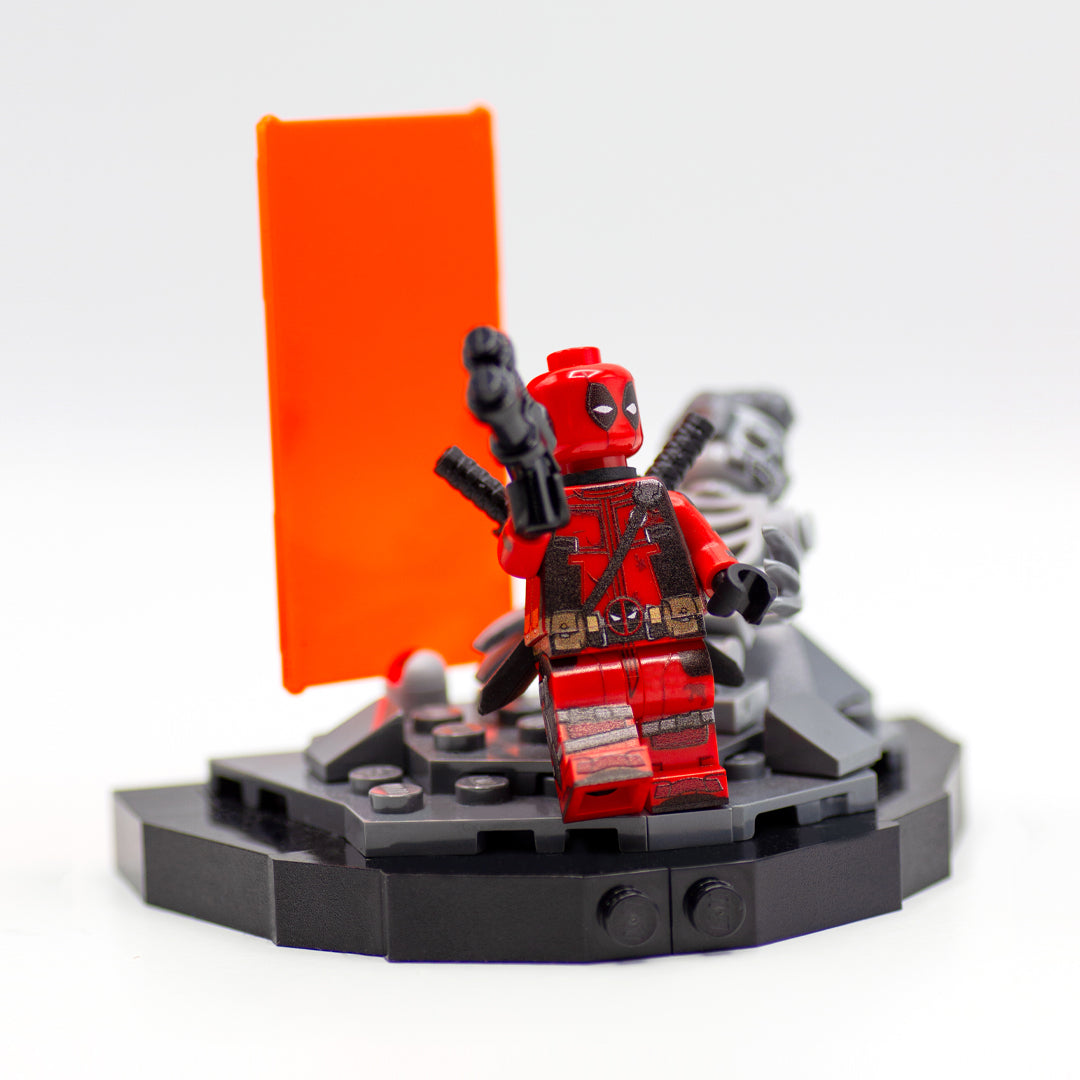 Minifigure inspired by Deadpool, standing on a custom LEGO display based on the scene from Deadpool and Wolverine movie, featuring orange Timedoor and the remains of Wolverine in LEGO form.