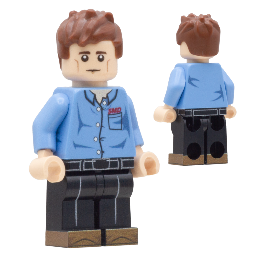 A toy minifigure shown from the front and back on a plain white background. The figure has brown hair, a beige face, a light blue button-up shirt with red 'SMD' lettering on the chest, black pants, and tan shoes.