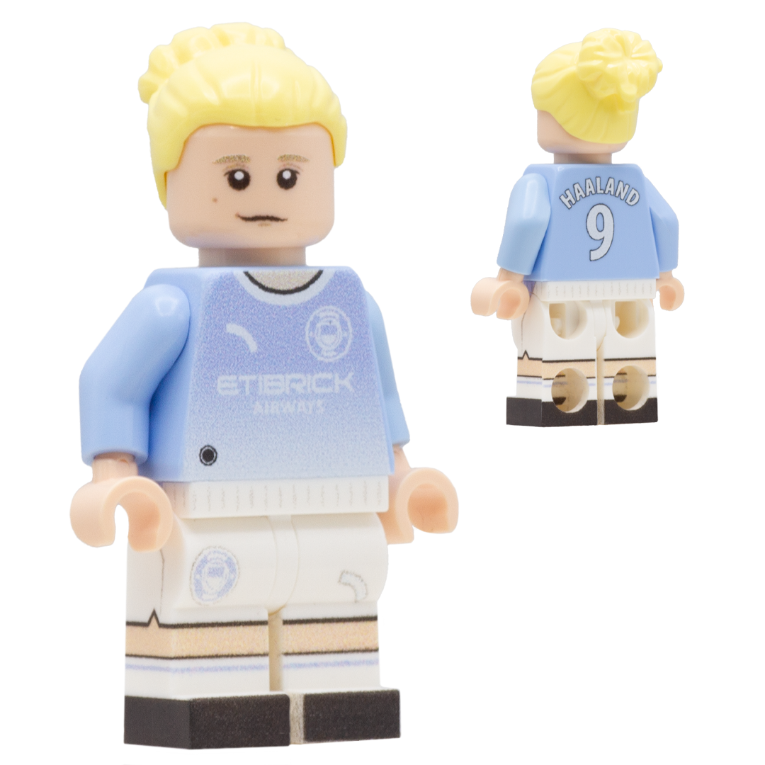 A LEGO minifigure depiciting Erling Haaland with blond hair, a light complexion face; wears a light blue and white Manchester City jersey with the text 'ETBRICK AIRPORT' on the front and 'HARLAND 9' on the back, along with white shorts and black-and-white striped socks.