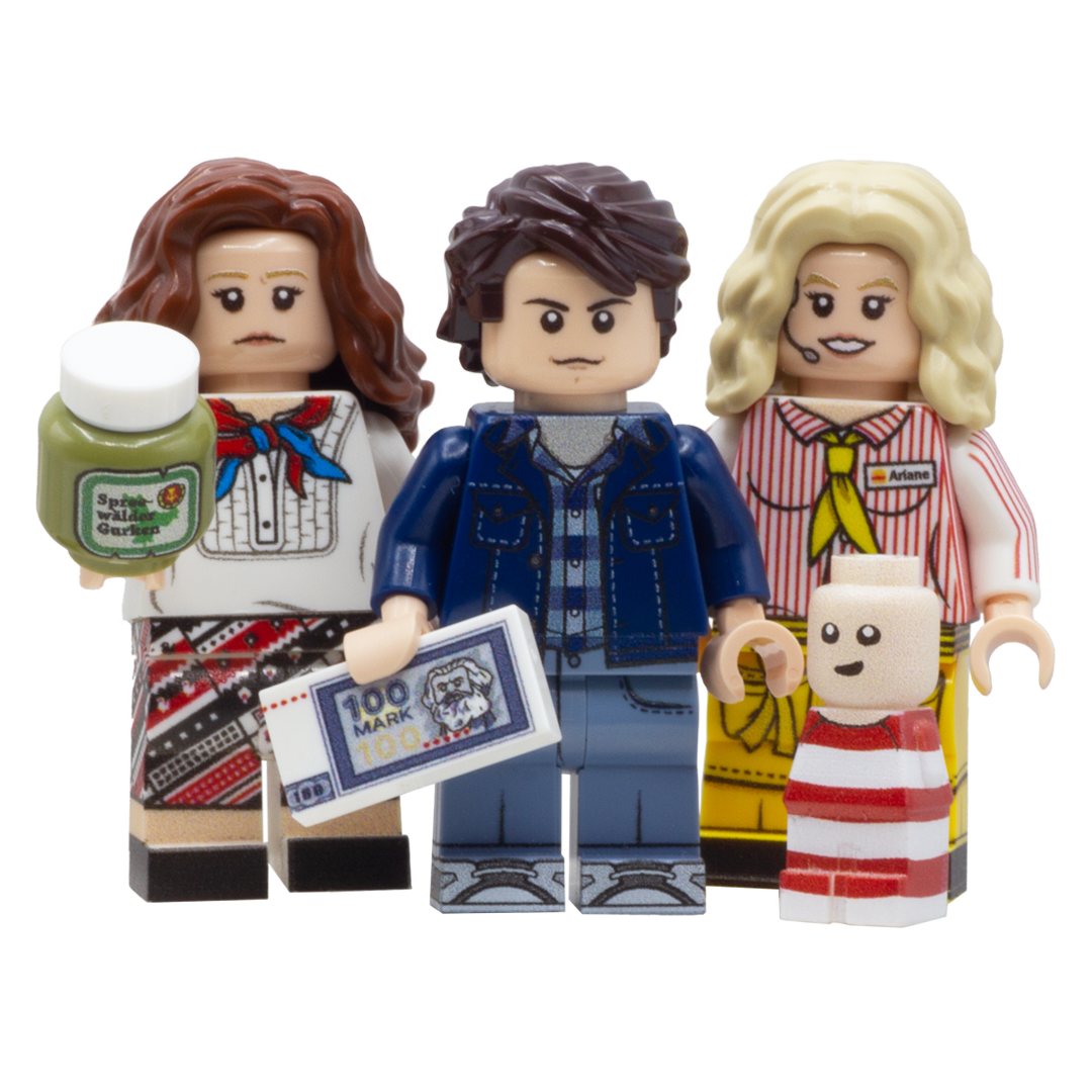 Three custom LEGO minifigures and a small baby figure, styled as characters from the film 'Good Bye Lenin' - mother holds a jar of pickles, Alex holds a 100 mark note and Ariane is dressed in her fastfood restaurant uniform.
