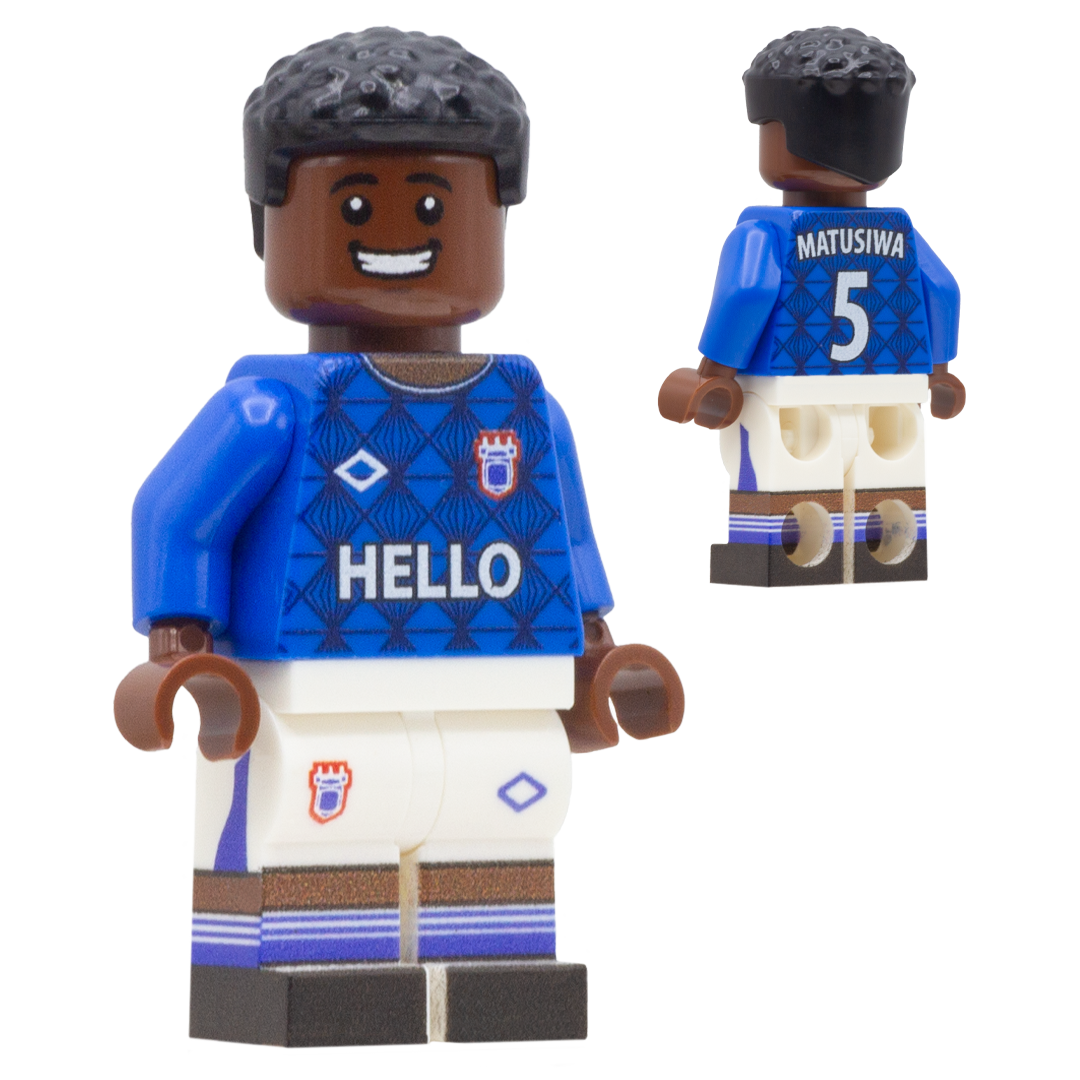 A football toy minifigure of Ipswich Town FC footballer Azor Matusiwa. The figure wears a blue jersey with 'HELLO' across the chest, a crest on the right chest, and 'MATUSIWA 5' on the back, paired with white shorts and brown socks.