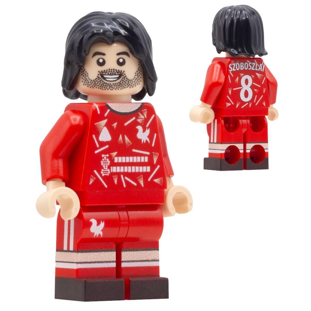 A red LEGO-style soccer minifigure of Liverpool FC footballer, Dominik Szoboszlai. The front view shows a smiling face, black hair, beard, red jersey with white graphic patterns, matching red shorts.