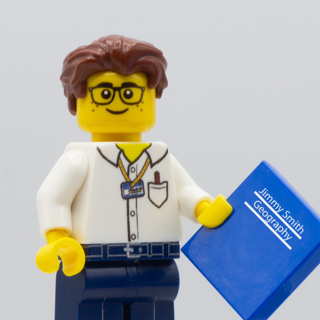 Custom LEGO Minifigure Teacher holding a personalised exercise book as a blue minifigure tile (text on the book reads Jimmy Smith, Geography)