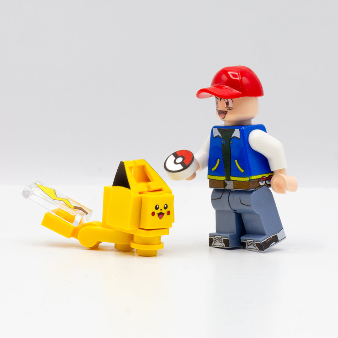 Custom-printed LEGO minibuild inspired by Pikachu standing next to a Pokémon trainer, Ash, custom LEGO minifigure wearing red cap and holding a small round tile with a Pokémon ball design printed on it.