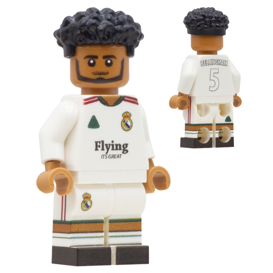 A soccer minifigure of Real Madrid footballer, Jude Bellingham. The figure has black curly hair, brown skin, and wears a white Real Madrid jersey with green and red accents, plus matching white shorts.