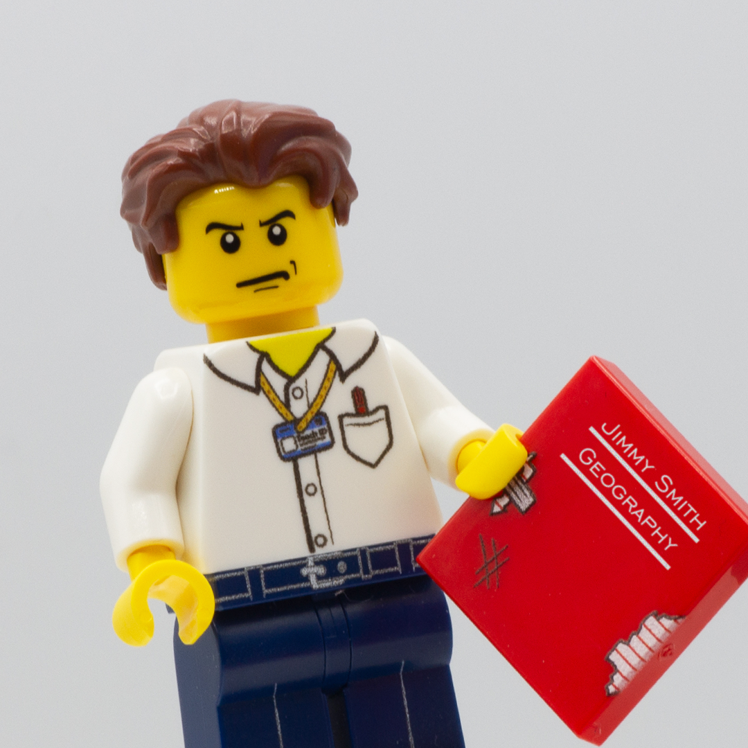 Custom LEGO Minifigure of a cross looking teacher holding a red lego tile which serves as a scruffy exercise book (text on the book reads Jimmy Smith, Geography)