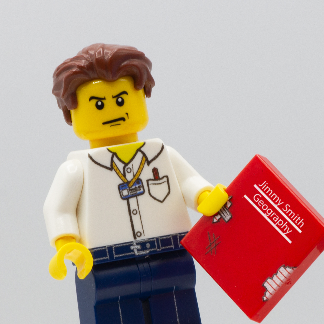 Custom LEGO Minifigure of a cross looking teacher holding a red lego tile which serves as a scruffy exercise book (text on the book reads Jimmy Smith, Geography)