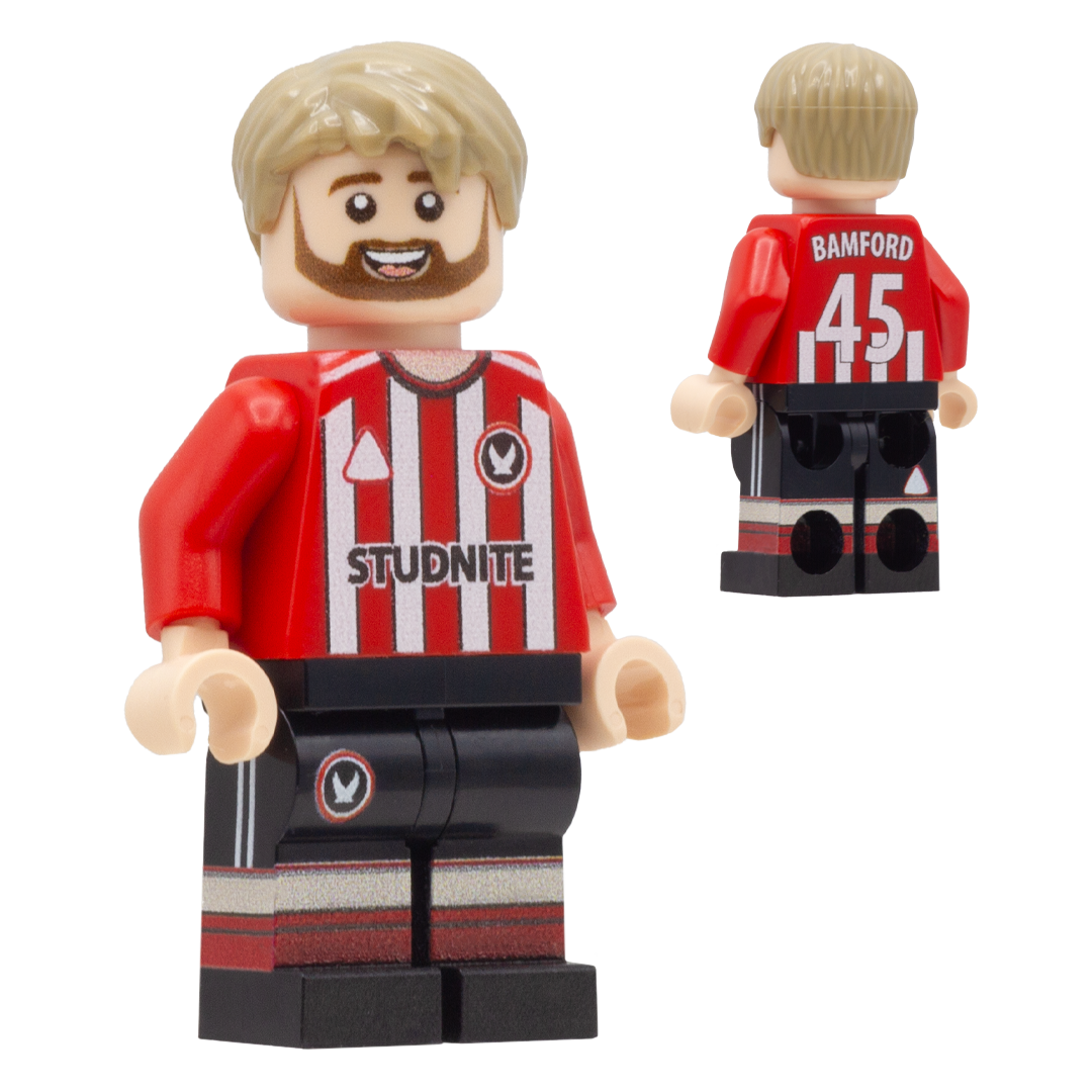 A LEGO-style football minifigure of Sheffield United footballer, Patrick Bamford. The figure has blond hair and a beard, wearing a red and white striped jersey with 'BAMFORD 45' and a circular crest, plus black shorts with red and white striping.