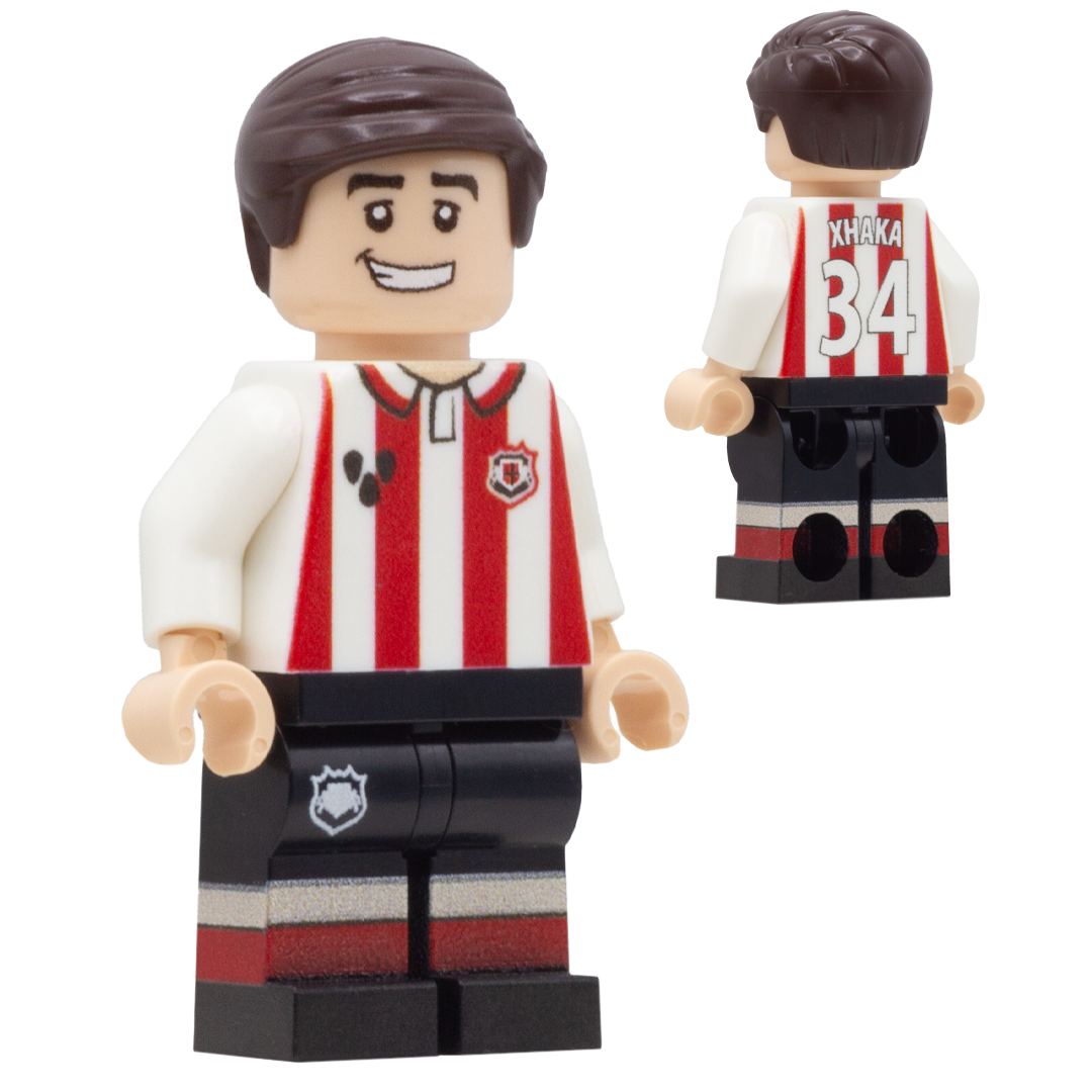 A LEGO-style soccer minifigure of Sunderland FC footballer, Granit Xhaka. The figure wears a red-and-white vertically striped jersey, black shorts with red and white stripes, and brown hair.