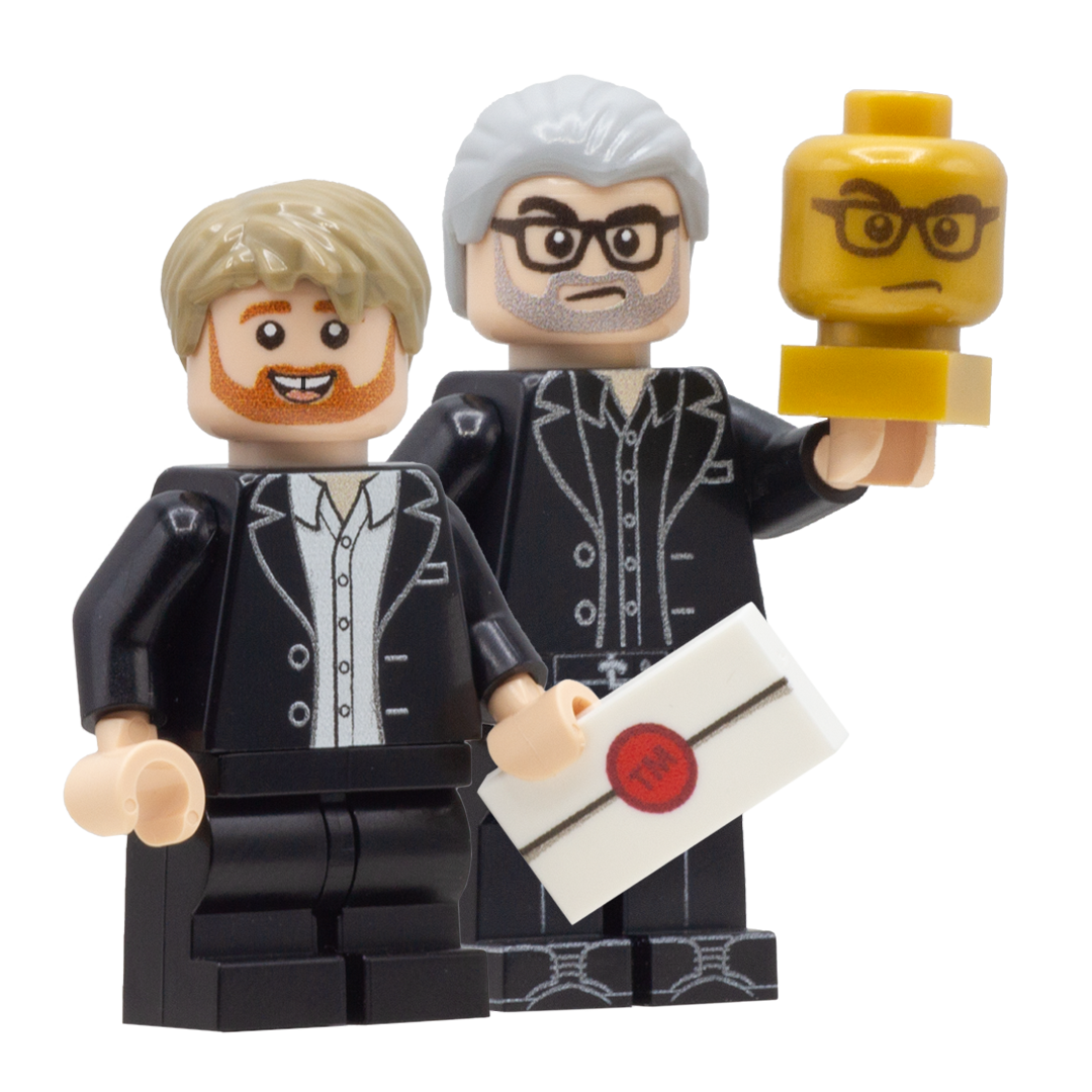 Custom LEGO minifigures of Alex Horne and Greg Davies from taskmaster - Alex holds a white LEGO tile with a red seal designed to look like a task, and Greg holds a gold LEGO head with his face on it. 