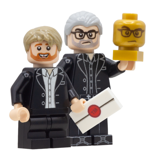 Custom LEGO minifigures of Alex Horne and Greg Davies from taskmaster - Alex holds a white LEGO tile with a red seal designed to look like a task, and Greg holds a gold LEGO head with his face on it. 
