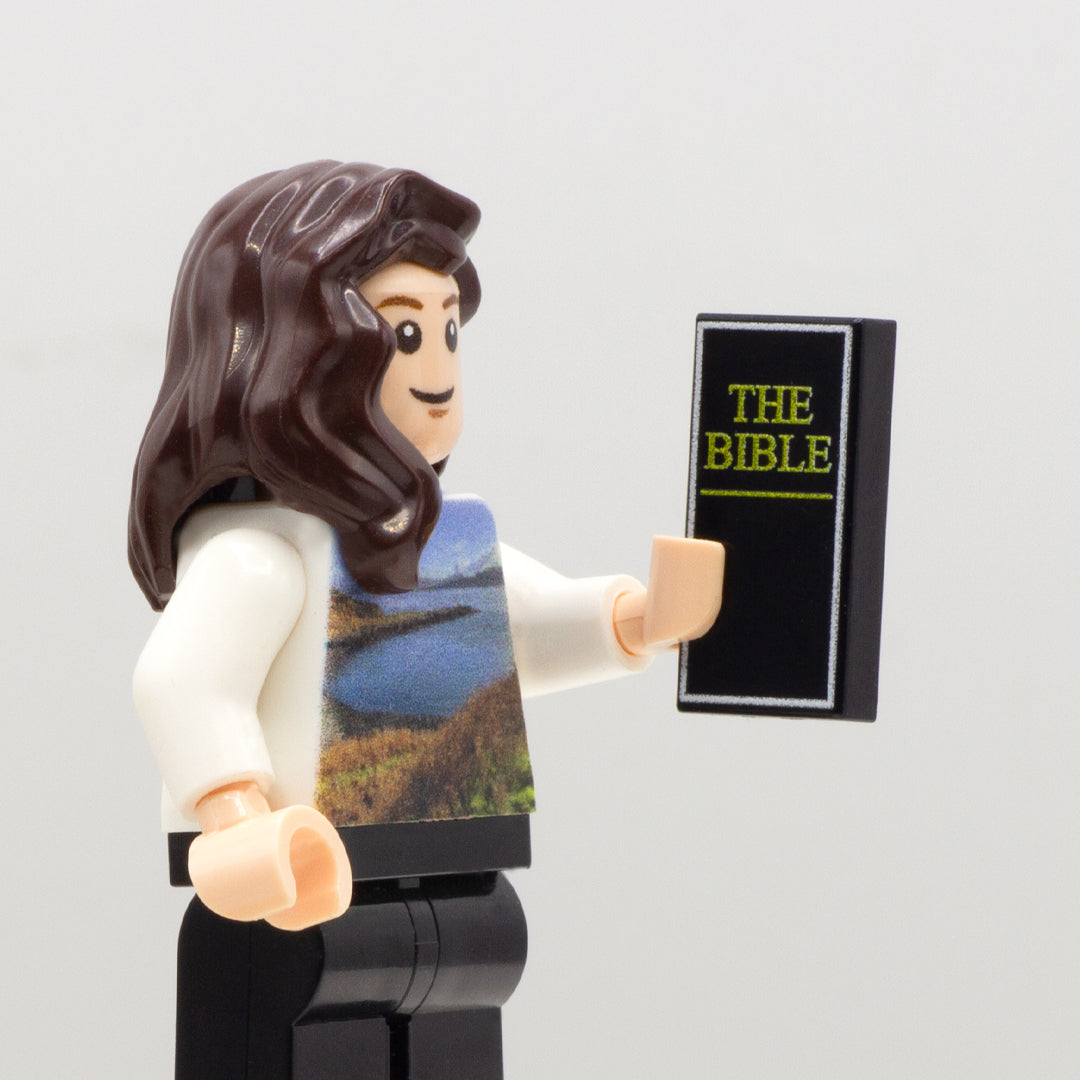 LEGO minifigure holding a custom black LEGO tile with The Bible title printed on it.