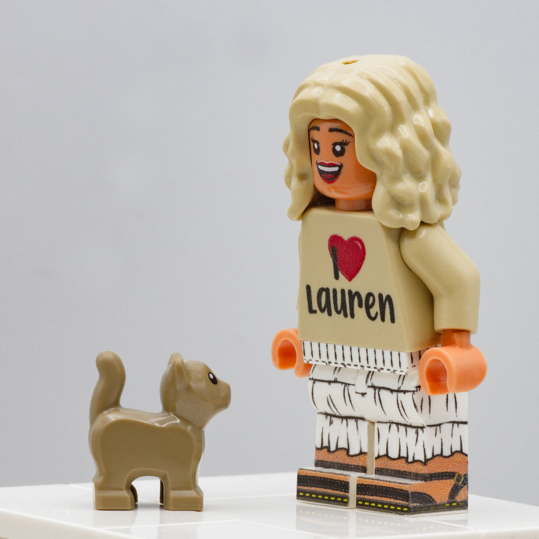 A light brown kitten LEGO accessory and a smiling LEGO minifigure in a skirt standing next to it for size comparison.