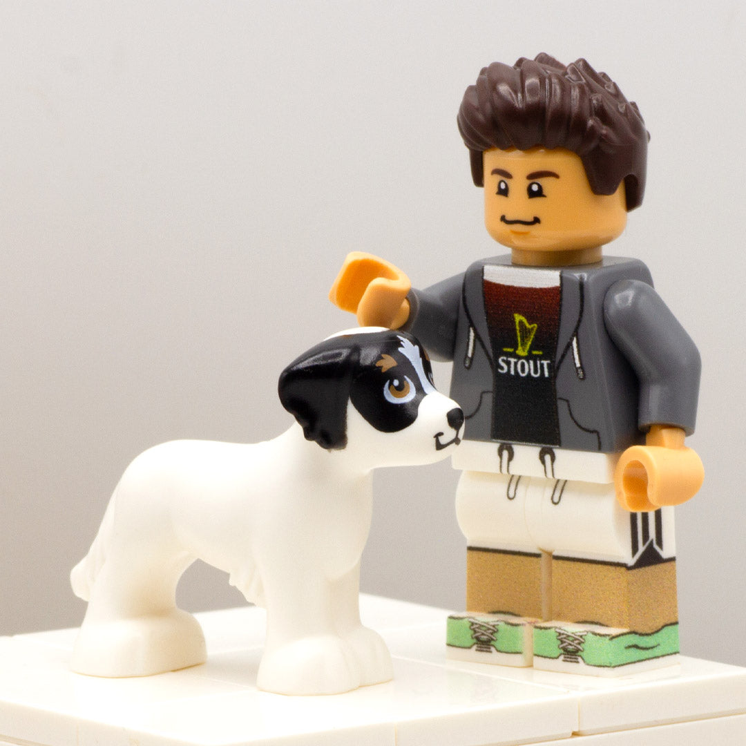 Minifigure standing next to LEGO white dog with brown eyes and, cute smiley face and black marks around eyes and ears.