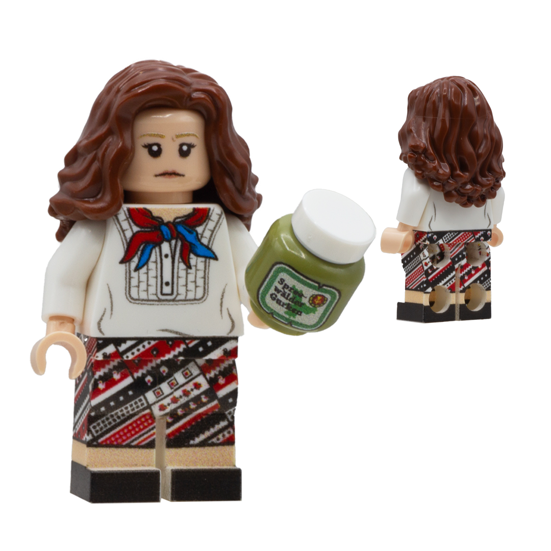 A custom LEGO female minifigure with brown wavy hair, a white shirt with a red and blue bow, and a red, black, and white patterned skirt. She is holding a small green jar of pickles, labelled in German, and is shown in both front and back views against a white background.