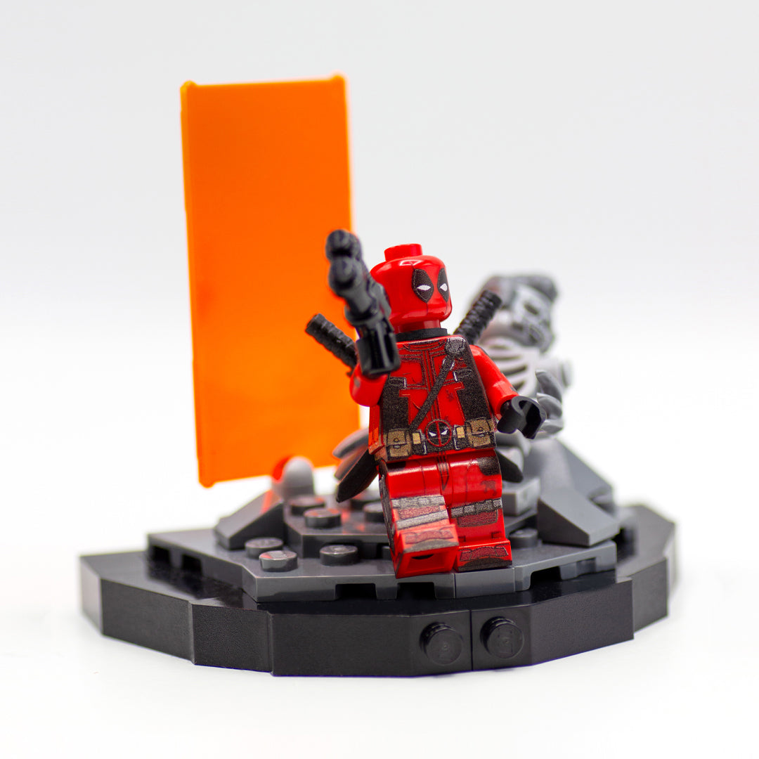 Minifigure inspired by Deadpool, standing on a custom LEGO display based on the scene from Deadpool and Wolverine movie, featuring orange Timedoor and the remains of Wolverine in LEGO form.