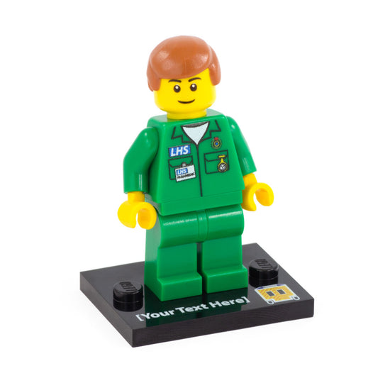a custom lego minifigure dressed as a paramedic with brown hair and closed smile, standing on a custom text baseplate with a printed ambulance symbol